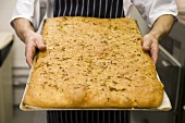 Man holding herb bread on baking tray