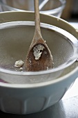 A baking bowl, sieve and wooden spoon with baking scraps