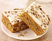 Two pieces of carrot cake with cream cheese icing & walnuts