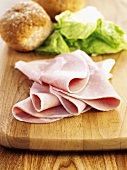 Wiltshire ham with lettuce and bread roll on wooden board