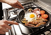 Man frying an English breakfast in a frying pan