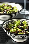 Two bowls of lettuce with roasted vegetables and olives