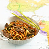 Strips of beef, vegetables, baby corn & sesame seeds on map (Asia)