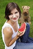 Junge Frau mit Wassermelone sitzt im Gras mit einem Hund