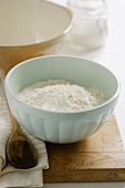 Flour in mixing bowl and wooden spoon on chopping board