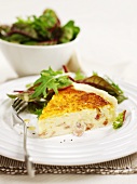 A piece of cheese and bacon quiche with side salad