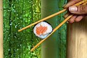 A hand holding a maki sushi in chopsticks