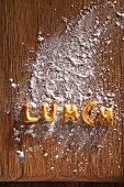 The word 'LUNCH' made out of pastry on a floured wooden board