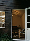 Blick durch geöffnete Tür eines Holzhauses in beleuchtetes Schlafzimmer mit Bett & Kuhfell