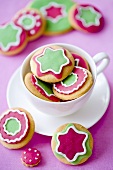 Assorted colorfully decorated Christmas cookies in and next to a teacup
