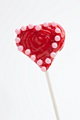 A red heart-shaped cake pop with pink sugar beads