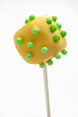 A yellow dice-shaped cake pop with green sugar beads