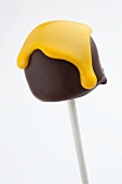 A cake pop shaped like a mini chocolate marshmallow with yellow icing