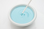 A stick dipped in a bowl of blue icing
