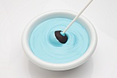 A cake pop being dipped into blue icing