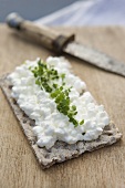 A crisp bread topped with cottage cheese and rocket on a wooden board