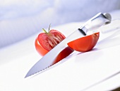 A halved tomato with a kitchen knife