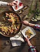 A person helping themselves to paella from a large pan