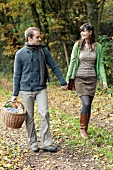 A couple with a picnic basket walking on the edge of a forest in autumn