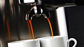 Kaffee fliesst aus der Maschine in zwei Tassen