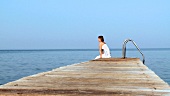 Young woman walking along landing stage and sitting down