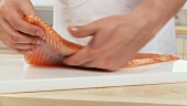 A fillet of salmon and a pair of hands removing the bones