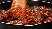 Bolognese sauce being stirred in a pan