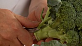 Leaves being removed from broccoli and the florets being cut off