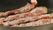 Rashers of bacon being fried in a pan