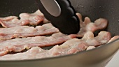 Rashers of bacon being fried in a pan