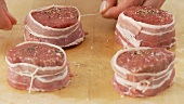 Beef fillet slices wrapped in bacon being secured with kitchen twine