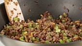 Minced meat being mixed in a pan with diced vegetables