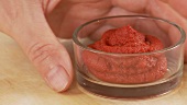 A hand taking a dish of tomato puree
