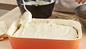 Lasagne sheets and Bechamel sauce being layered in a baking dish