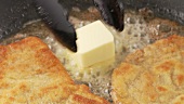 Panierte Schnitzel in einer Pfanne braten, ein Stück Butter in die Pfanne geben