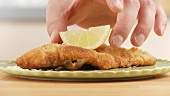Escalope á la viennoise being garnished with a slice of lemon