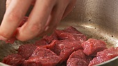 Pieces of meat being placed in a pot