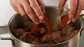 Goulash meat being dusted with paprika and stirred