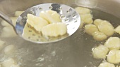 Gnocci being removed from salt water with a draining spoon