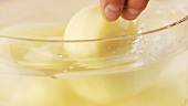 Peeled potatoes being placed in a bowl of cold water