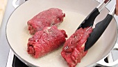 Beef roulade being placed in a frying pan of hot oil