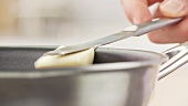 A piece of butter being placed in a pan