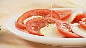 Tomato and mozzarella slices being drizzled with olive oil