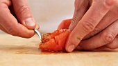 A peeled tomato being quartered and deseeded
