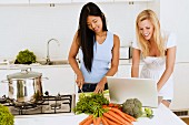Two young women cooking and using laptop