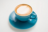 A cappuccino in a blue cup with a milk foam heart