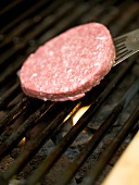 A raw burger being place on a barbecue