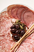 A meat platter with olives, capers and bread sticks (Italy)