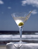 Glas Martini mit grüner Olive, Hintergrund: Meeresstrand