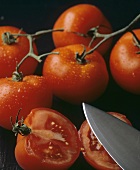 Frische ganze Tomaten und halbierte Tomate mit Messerspitze